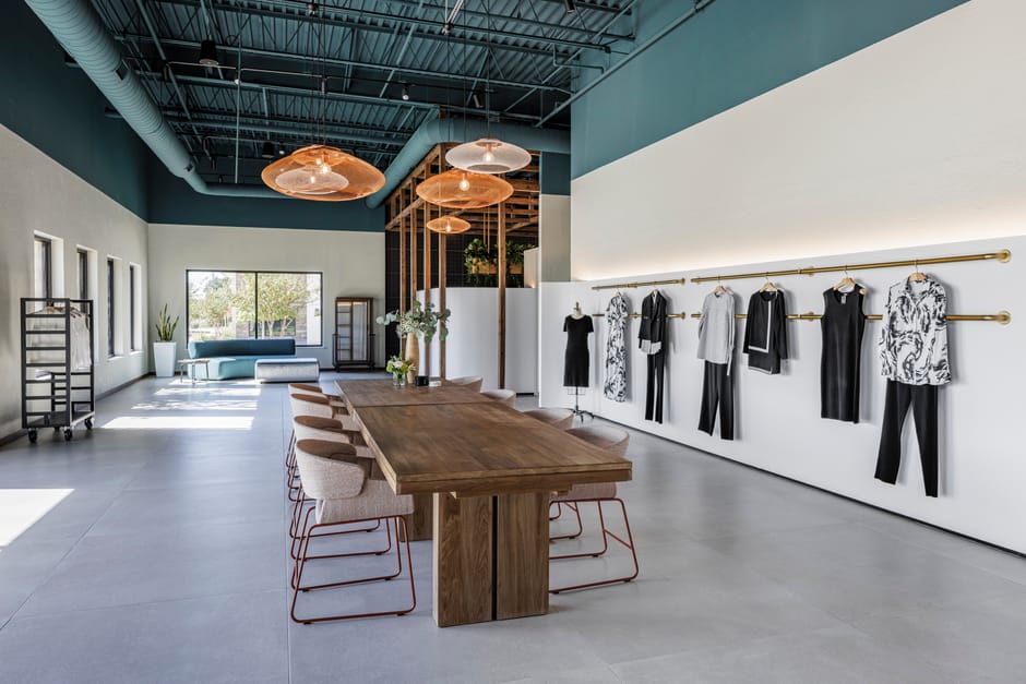 Main showroom with long wood table, brass display rails, and teal ceiling